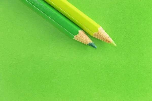 Two green  pencils on a colored  background , light green and dark green on a green background ,beautiful monochromatic effect