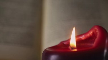 Işıklı mum altında okuma , ön planda bir kırmızı mum, arka planda odak dışında açık bir kitap