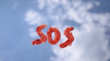  Aynada turuncu rujla yazılmış SOS mesajı, aynada mavi bulutlu gökyüzü yansıyor, güzel beyaz bulutlar hızla akıyor 