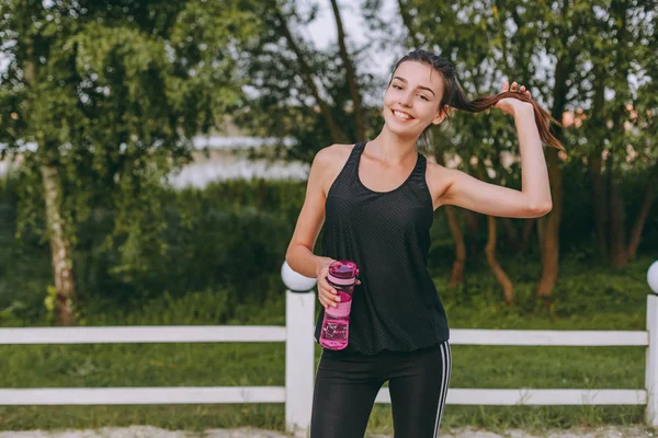 Dehidratasyon kavramı. Portre sevimli esmer kadın atlet içme suyu plastik şişe koşu sonra uygun. Güzel kız kardiyo eğitim açık havada sonra susuzluğunu spor giyim.