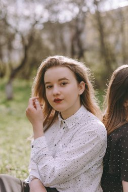 Kız gülümseyerek oturan ve yeşil bahar bahçesinde kız kardeşi üzerine eğilerek, güneş alanında sarılma. Birlikte eğlenmek, olumlu duygular, parlak renkler. Gün batımında mutlu kız arkadaşları