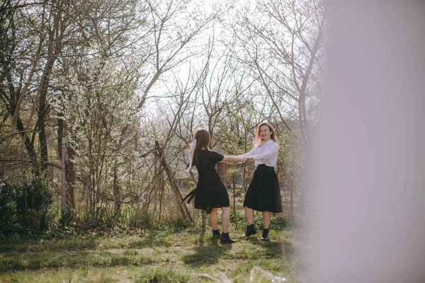 Dancing lyckliga flickvänner. Porträtt av två vackra unga systrar i den gröna vårträdgården, kramas i fältet i solskenet. Ha kul tillsammans, positiva känslor, ljusa färger. Kopiera utrymme — Stockfoto