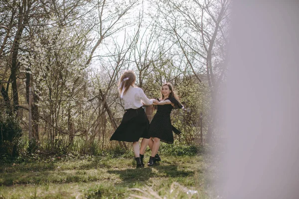 Dancing lyckliga flickvänner. Porträtt av två vackra unga systrar i den gröna vårträdgården, kramas i fältet i solskenet. Ha kul tillsammans, positiva känslor, ljusa färger. Kopiera utrymme — Stockfoto