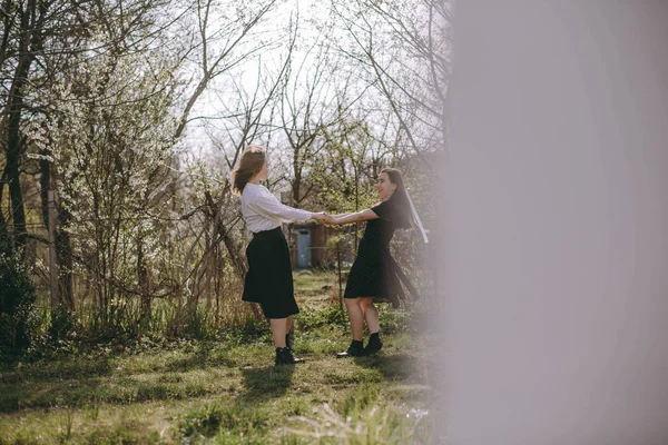 Dancing lyckliga flickvänner. Porträtt av två vackra unga systrar i den gröna vårträdgården, kramas i fältet i solskenet. Ha kul tillsammans, positiva känslor, ljusa färger. Kopiera utrymme — Stockfoto