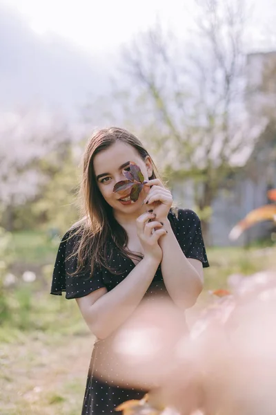 Portrét velmi krásné smyslné a brunetové dívky v černých šatech, upřímném úsměvu, v létě v zahradě na pozadí květin, mladé studentky v parku na jaře, slunečného dne — Stock fotografie