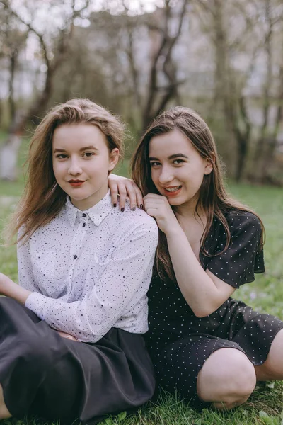 Портрет двох красивих молодих сестер, що сидять у зеленому весняному парку, обіймають у полі. Розважаючись разом, позитивні емоції, яскраві кольори. Копіювати простір. Щасливі подружки на заході сонця — стокове фото