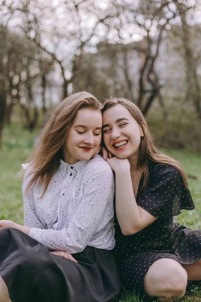 Yeşil bahar parkında oturan, tarlada sarılan iki güzel genç kız kardeşin portresi. Birlikte eğlenmek, olumlu duygular, parlak renkler. Kopya alanı. Gün batımında mutlu kız arkadaşları