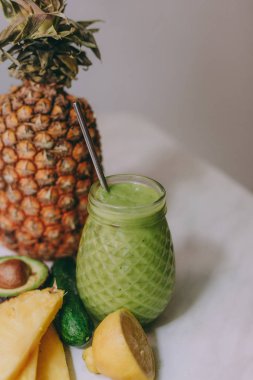 Beyaz bir masada limon, zencefil, avokado, salatalık ile yapılan ev yapımı ananas Smoothie