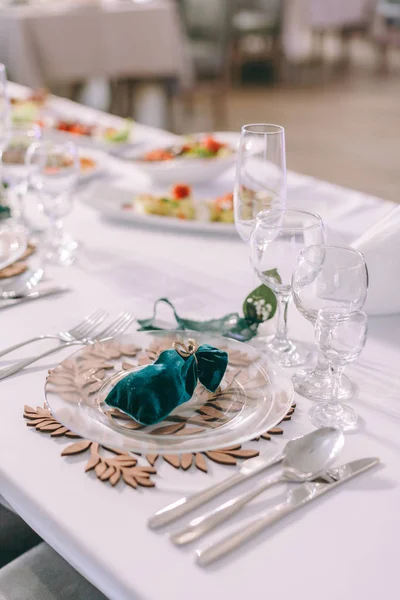 Table ronde de banquet servi. Intérieur du restaurant pour le dîner de mariage, prêt pour les invités. Décoré avec un arrangement floral. Concept de restauration. Compliment pour les invités sur une assiette sur une table côté serveur — Photo