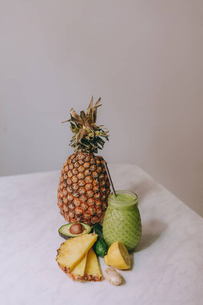 Homemade pineapple smoothie made with lemon, ginger, avocado, cucumber on a white table