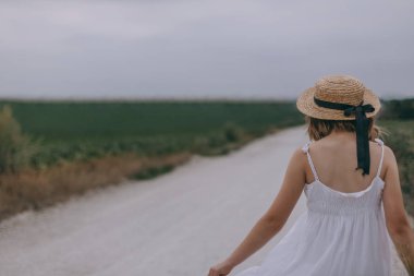 Beyaz elbise ve çizmeler içinde güzel bir genç kadın kırsal yolda yürüyor. Dans ediyor, eğleniyor ve özgürlük yayıyor.