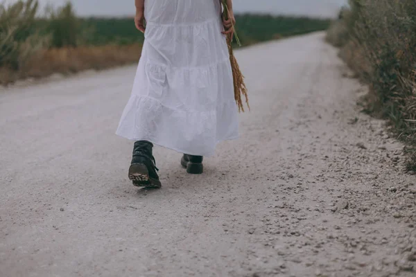 En vacker ung kvinna i en vit klänning och stövlar går landsbygdens väg. Hon dansar, har kul och utstrålar frihet — Stockfoto