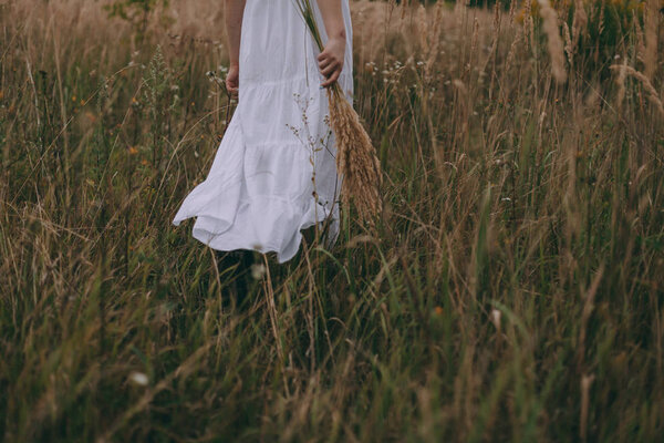A beautiful young woman in a white dress and boots walks rural road. She dances, has fun and radiates freedom