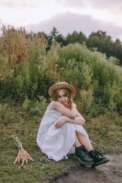 Krásná bohémské dívka, která sedí při západu slunce u jezera. atraktivní mladá žena v bílých šatech s větrnou srstí v blízkosti vody mezi zelenými listy. Letní dovolená — Stock fotografie