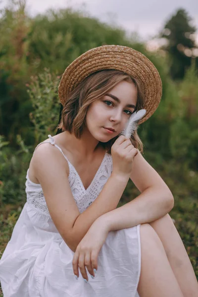 güzel boho kız göl yakınında gün batımı ışıkta oturan. yeşil yaprakları arasında su yakınında rahatlatıcı rüzgarlı saçları ile beyaz bohem elbiseli çekici genç kadın. yaz tatili