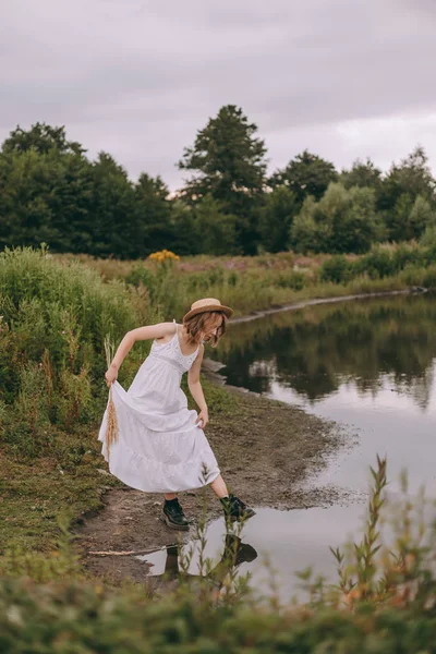 Pohled na krásnou mladou ženu s krátkými černými botami a bílými šaty, které se krojí do jezera — Stock fotografie