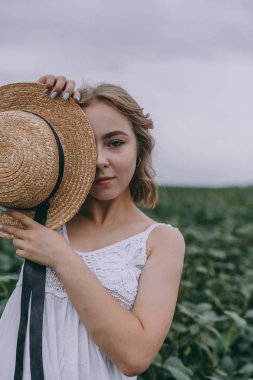 güzel kız bir şapka ile yüzünü kapatır. Rüzgarlı saçlı beyaz bohem elbiseli çekici genç kadın yaprakları arasında dinlenmeye devam ediyor. yaz tatili