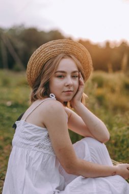 güzel boho kız göl yakınında gün batımı ışıkta oturan. yeşil yaprakları arasında su yakınında rahatlatıcı rüzgarlı saçları ile beyaz bohem elbiseli çekici genç kadın. yaz tatili