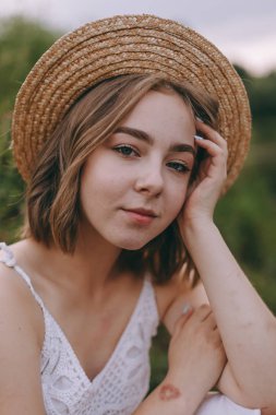 güzel boho kız göl yakınında gün batımı ışıkta oturan. yeşil yaprakları arasında su yakınında rahatlatıcı rüzgarlı saçları ile beyaz bohem elbiseli çekici genç kadın. yaz tatili