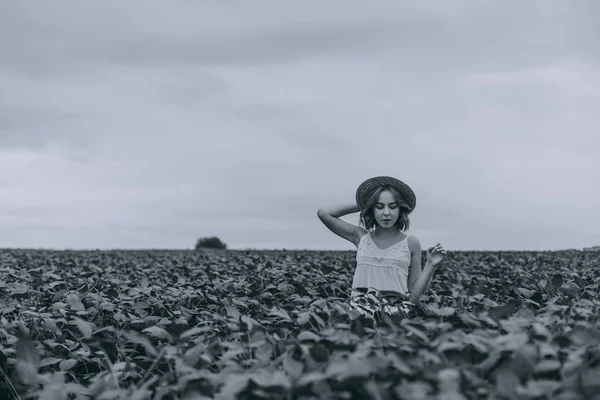 Krásná mladá dívka v bílých šatech a slaměném klobouku v zeleném poli s kyticí sušených bylin. černobílá fotografie — Stock fotografie