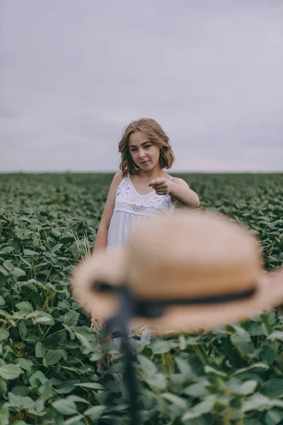 Krásná dívka při západu slunce držela v ruce klobouk a hodila ji do kamery. Léto, zábava a životní styl venku — Stock fotografie