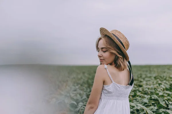 Schönes junges Mädchen in weißem Kleid und Strohhut im grünen Feld umarmt Strauß getrockneter Kräuter — Stockfoto