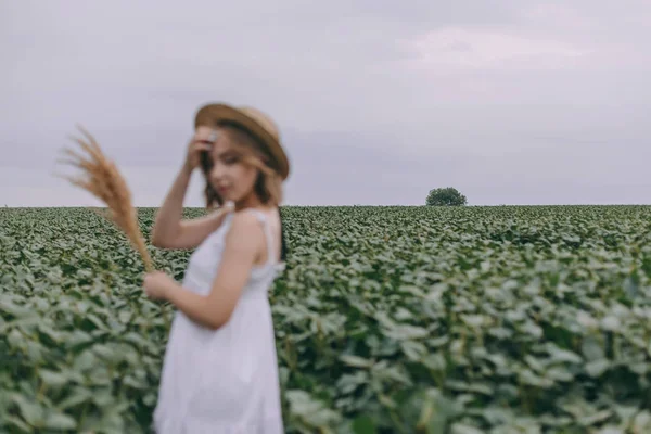 Krásná mladá dívka v bílých šatech a slaměném klobouku v zeleném poli — Stock fotografie