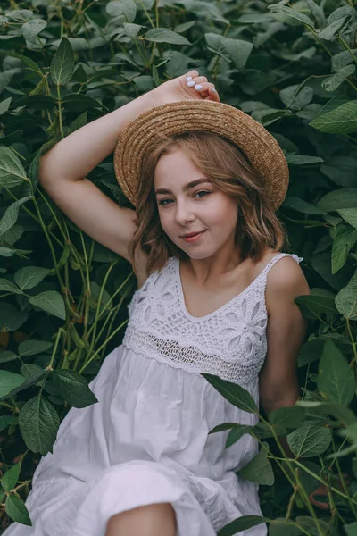 Schönes Mädchen auf einem Feld sitzend. attraktive junge Frau im weißen Bohème-Kleid mit windigen Haaren, die es sich zwischen Blättern gemütlich macht. Sommerferien — Stockfoto