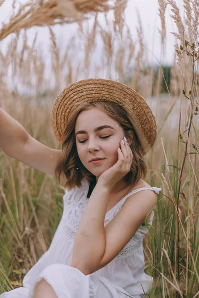 Schönes Mädchen auf einem Feld sitzend. attraktive junge Frau im weißen Bohème-Kleid mit windigen Haaren, die es sich zwischen Blättern gemütlich macht. Sommerferien — Stockfoto