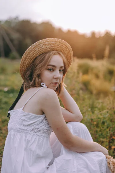 Schöne Boho Mädchen sitzt bei Sonnenuntergang Licht in der Nähe des Sees. attraktive junge Frau im weißen Bohème-Kleid mit windigen Haaren, die es sich am Wasser zwischen grünen Blättern gemütlich macht. Sommerferien — Stockfoto