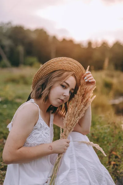 Schöne Boho Mädchen sitzt bei Sonnenuntergang Licht in der Nähe des Sees. attraktive junge Frau im weißen Bohème-Kleid mit windigen Haaren, die es sich am Wasser zwischen grünen Blättern gemütlich macht. Sommerferien — Stockfoto