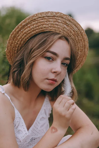 Schöne Boho Mädchen sitzt bei Sonnenuntergang Licht in der Nähe des Sees. attraktive junge Frau im weißen Bohème-Kleid mit windigen Haaren, die es sich am Wasser zwischen grünen Blättern gemütlich macht. Sommerferien — Stockfoto