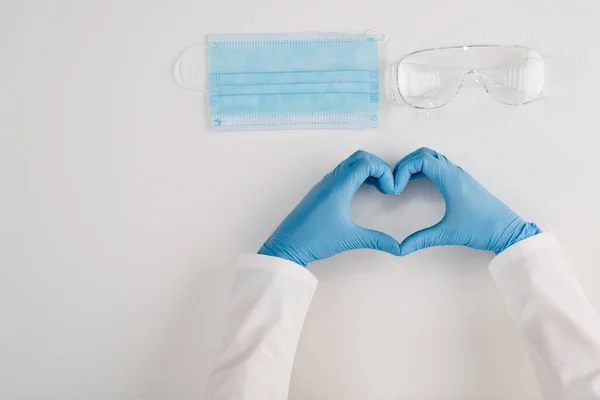 Medical protection for the public and health workers. Top view of a mask, gloves, goggles against pandemic virus. Heart from the hands of a blue glove on a white background.