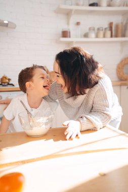 Anne ve oğlu evde hafif bir arka plan mutfağında hamur işinden un pişiriyorlar. Kadın ve erkek çocuk hamura bulanmış gülüyorlar..