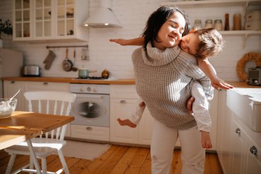 Parlak bir mutfağın arka planında anne, onu sırtında tutan bir bebekle uçak çalarken eğleniyor. Oğlu kendini genç bir kadının kollarında bir pilot olarak temsil ediyor..