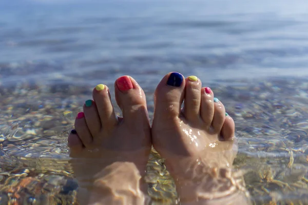 legs with multi-colored pedicure in clear water in the bright sun