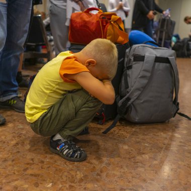 Sarışın çocuk havaalanında rötarlı bir uçuş beklemekten bıktı, bavulun yanında çömeldi.