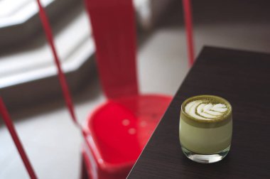 Ahşap plaka ve kırmızı sandalye üstten görünüm sıcak matcha kahve mocaccino cappuccino latte sanat seramik Kupası'nda. Matcha Kupası en iyi görünümü tablo. Kafede çay bardağı. Güzel yeşil köpük; Cam bardak; şık tonlama; metin için yer.