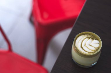 Ahşap plaka ve kırmızı sandalye üstten görünüm sıcak matcha kahve mocaccino cappuccino latte sanat seramik Kupası'nda. Matcha Kupası en iyi görünümü tablo. Kafede çay bardağı. Güzel yeşil köpük; Cam bardak; şık tonlama; metin için yer.