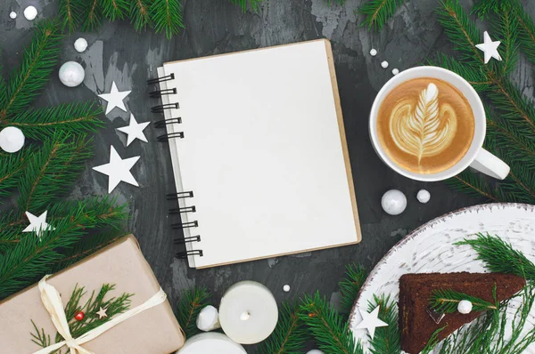 Beautiful christmas composition of notebook, cup of coffee, cake and gift on back table. Flat lay, top view, copy space