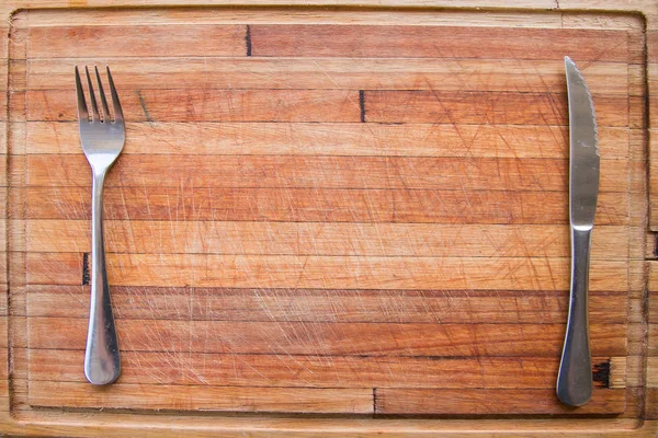 knife and silver fork on a wooden cutting board