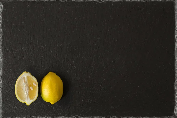 lemon sliced on a black slate background with garden green garnish