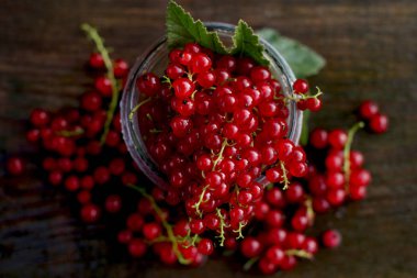 Su damlacıkları ile ahşap bir arka plan üzerinde yeşil yaprakları ile cam bir kavanozda kırmızı kuş üzümü