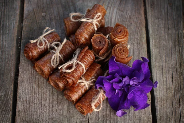 Handmade apple pastille twisted and tied with linen thread on a wooden background with petunia flowers