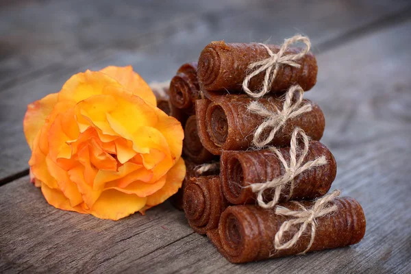 Handmade apple pastille rolled and tied with linen thread on a wooden background with an orange rose
