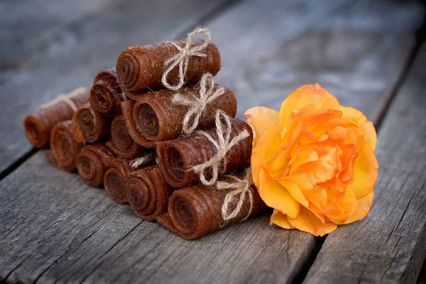 Handmade apple pastille rolled and tied with linen thread on a wooden background with an orange rose