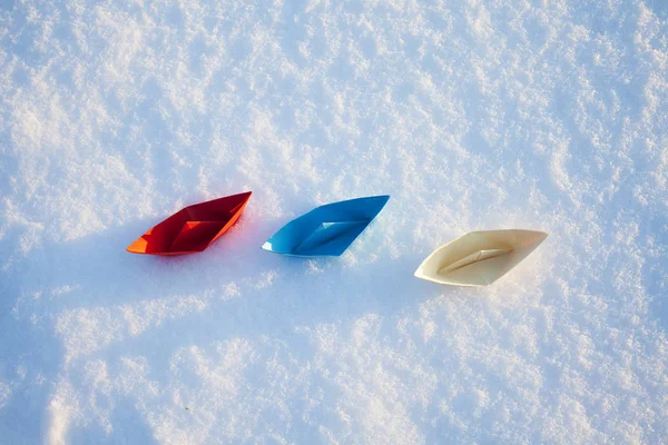 Red, blue and white paper boat in the snow. Winter
