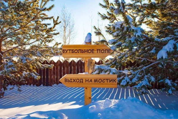 Direction indicator made of wood. Winter landscape. Snow and spruce. The inscription on the sign in Russian \