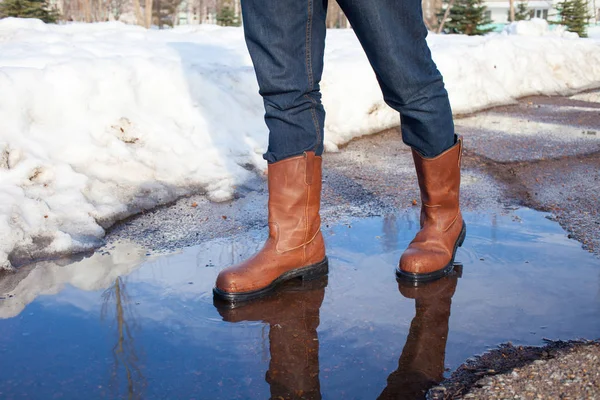 A man in leather boots is on puddles in early spring. Puddles, m