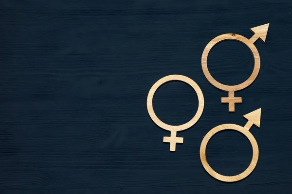 A symbol of gender equality made of plywood. Black wooden background. Male and female symbols